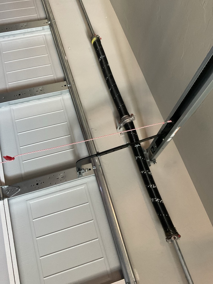 New black garage door spring installed on white garage door frame